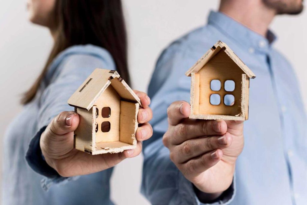A separated couple each holding a miniature house, representing the division of assets and property in family law disputes managed by Judith Ramos, Attorney at Law in Fort Lauderdale, Florida.