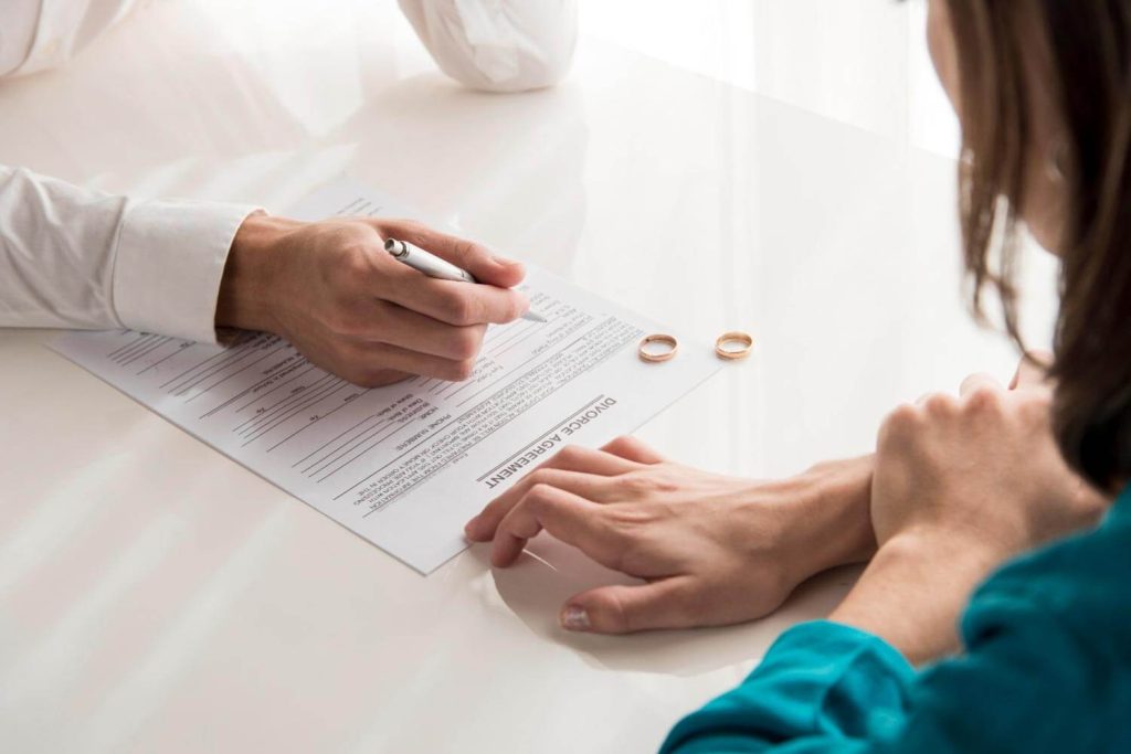 A couple signing divorce papers in Fort Lauderdale, Florida, with their wedding rings set aside, representing the professional support provided by Judith Ramos, Attorney at Law in divorce cases.