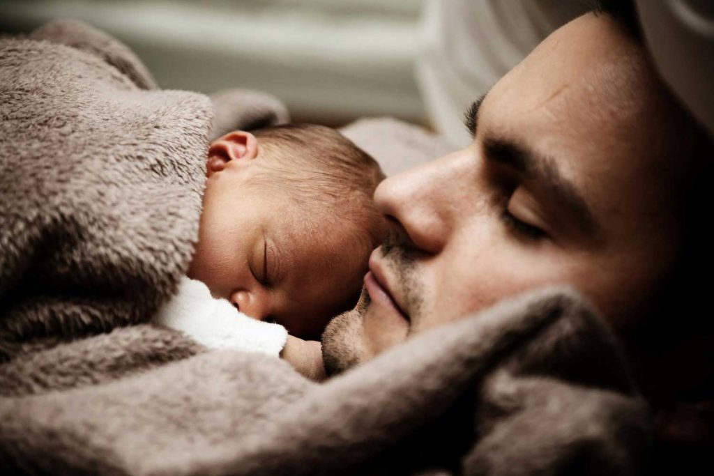 A tender moment with a father sleeping next to his newborn baby, representing the close bond and responsibility in fatherhood, an important element in family law cases managed by Judith Ramos, Attorney at Law in Fort Lauderdale, Florida.